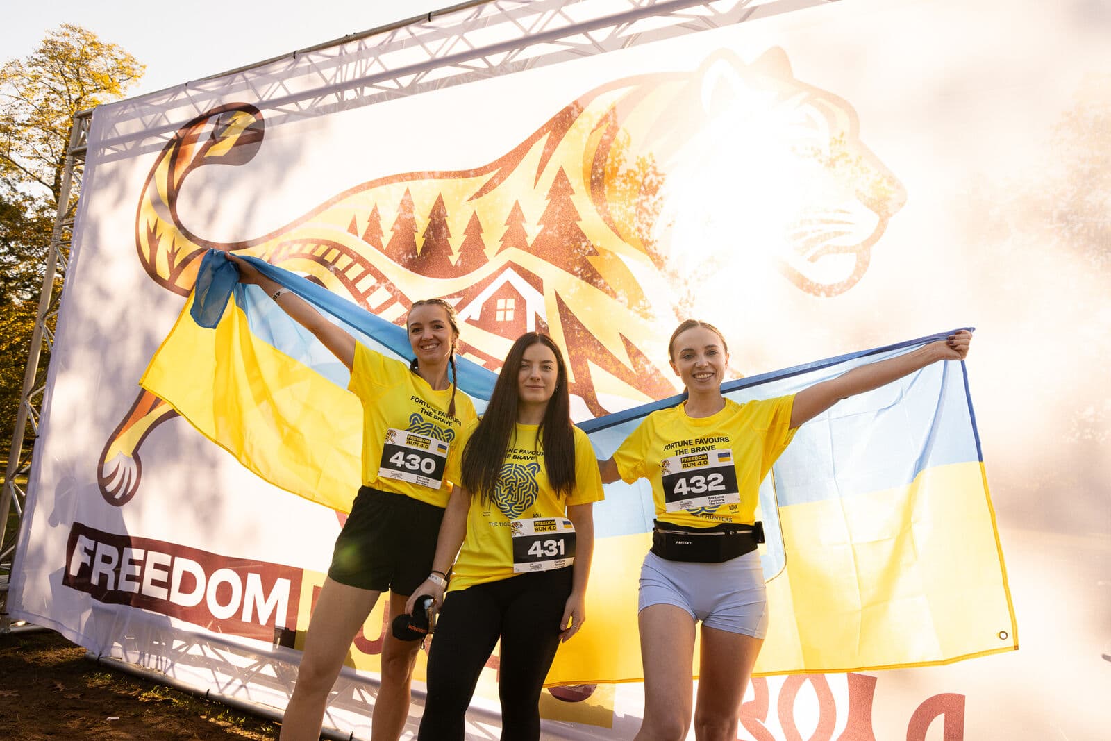 Three runners holding Ukrainian flags in front of the Freedom Run 4.0 banner