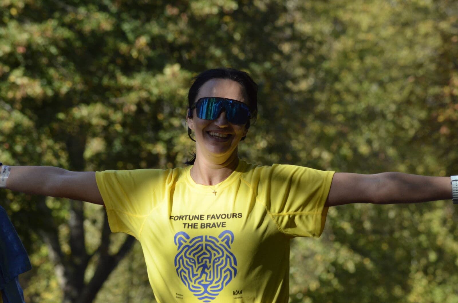 A runner with arms spread wide on the tree-lined course